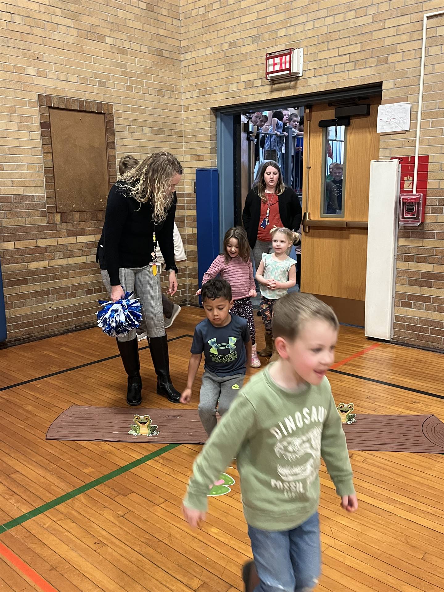 student between 2 adults leaping over a paper log.