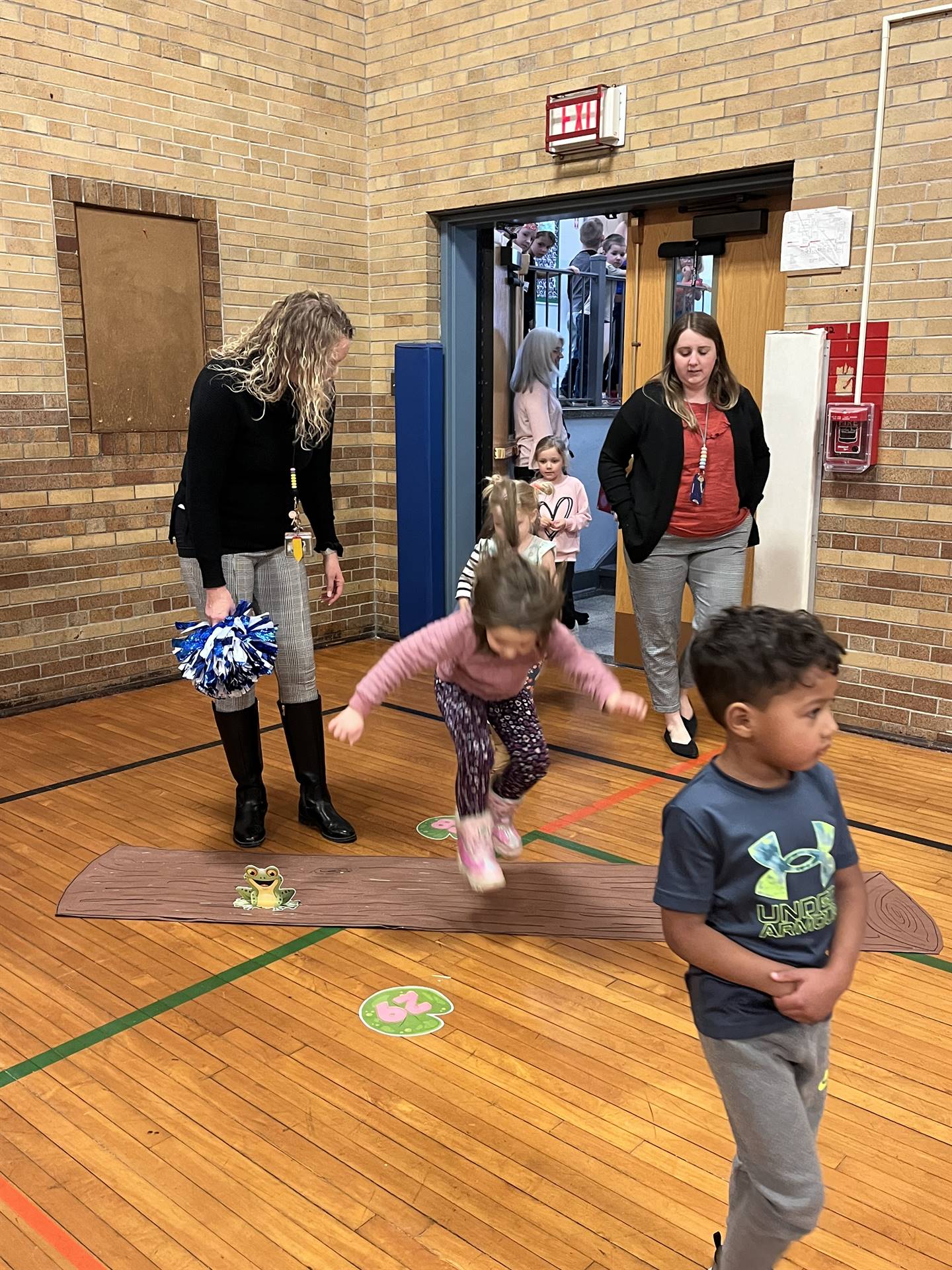 student between 2 adults leaping over a paper log.