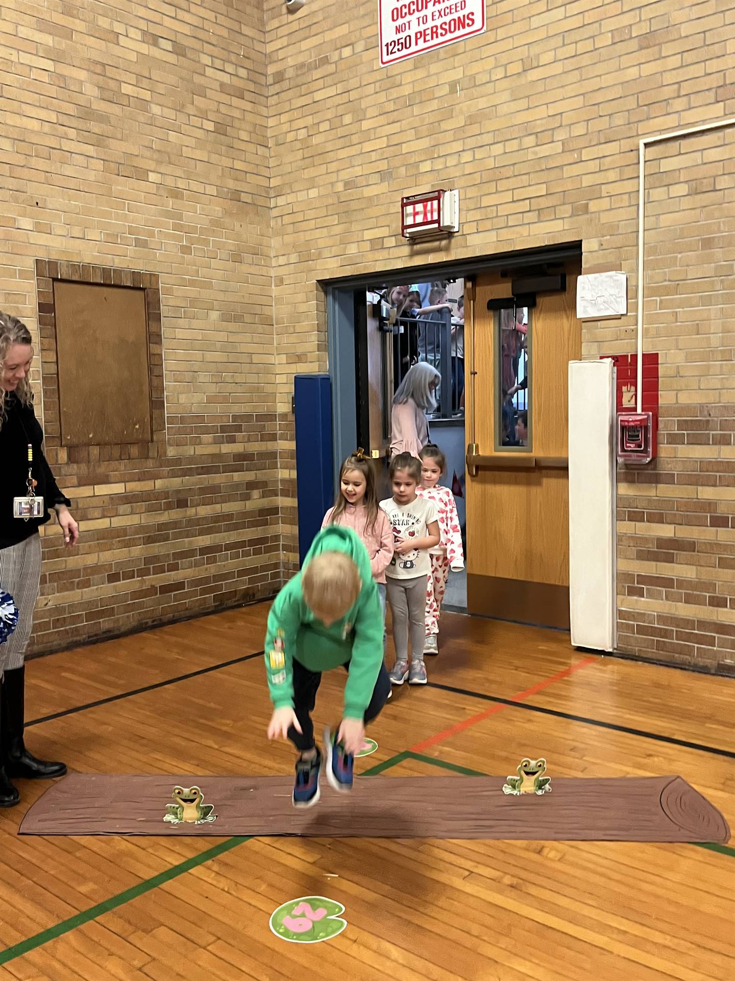 student between 2 adults leaping over a paper log.