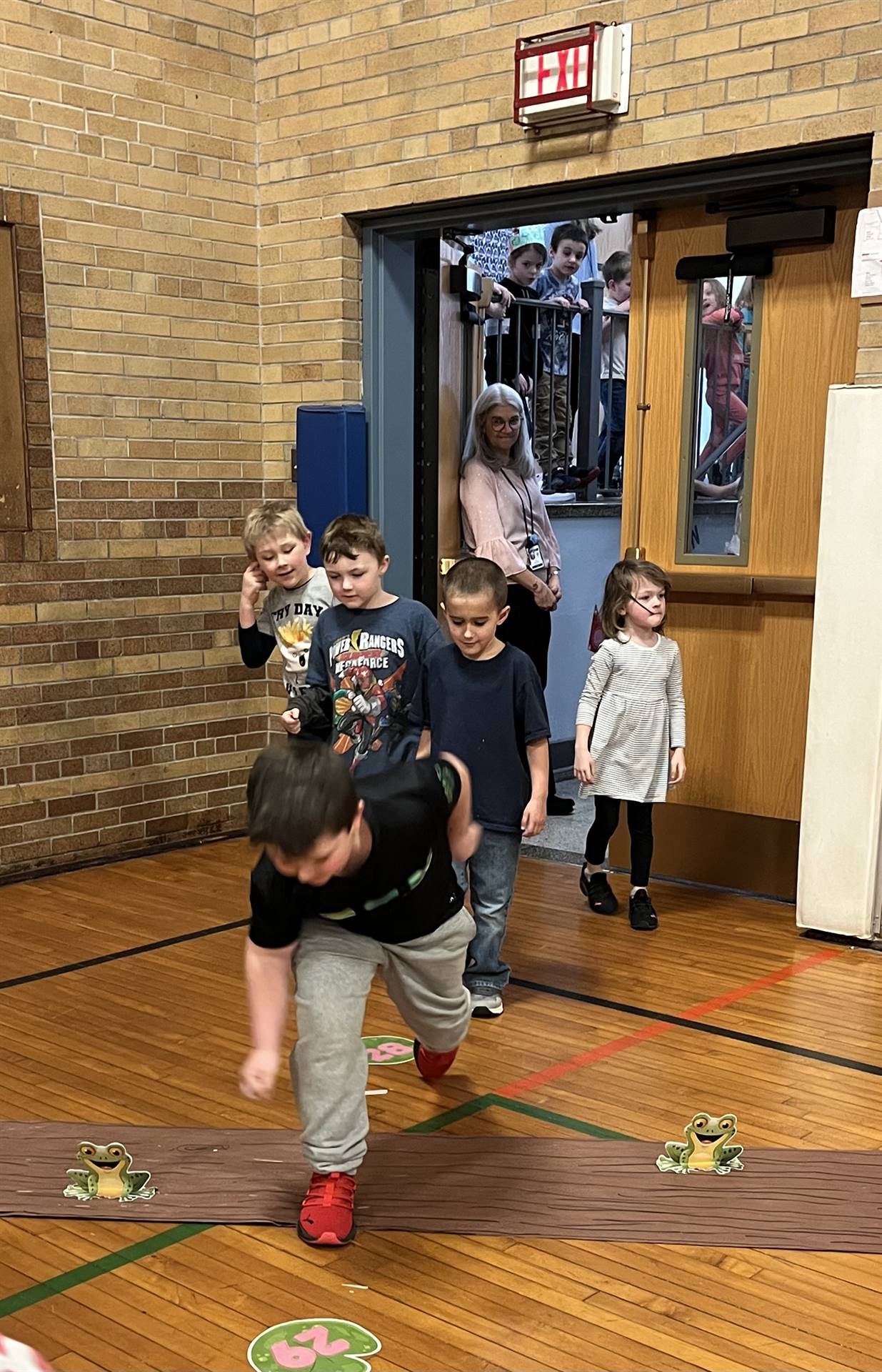 student between 2 adults leaping over a paper log.