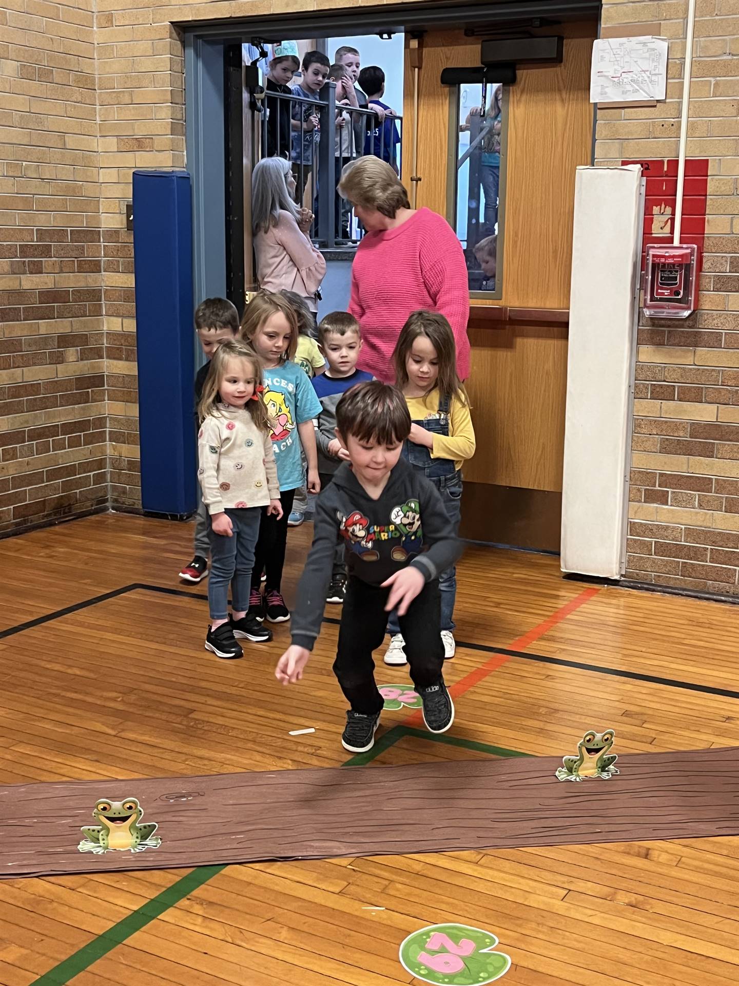 student between 2 adults leaping over a paper log.