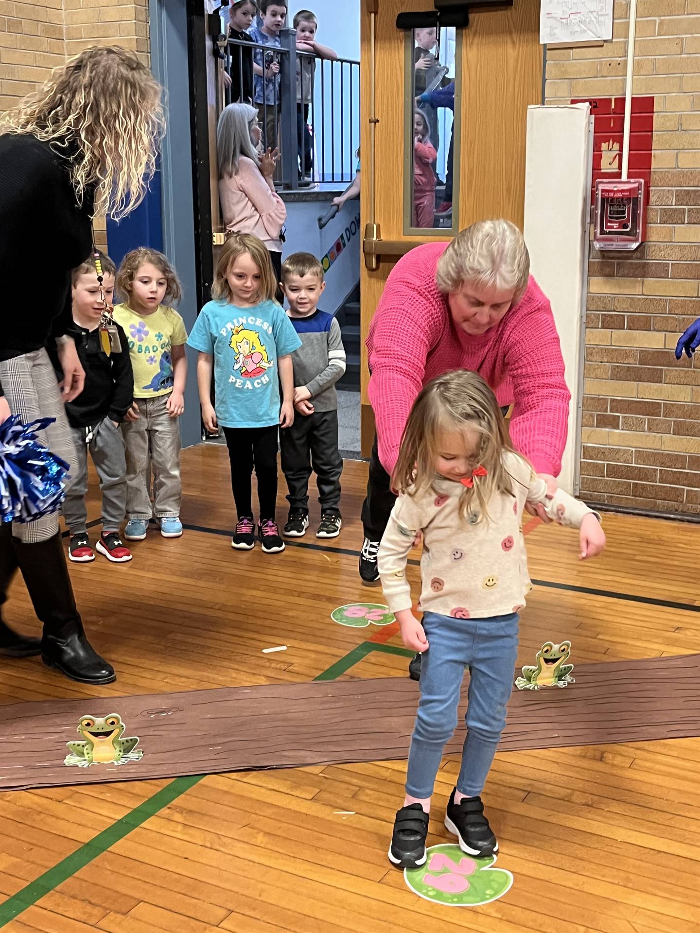 adult helping a student leap over a paper log.