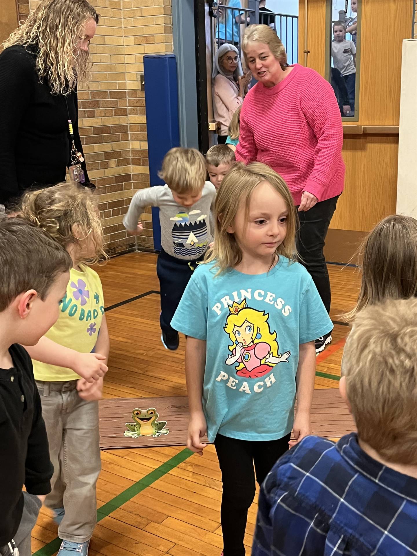 student between 2 adults leaping over a paper log while other student enter gym