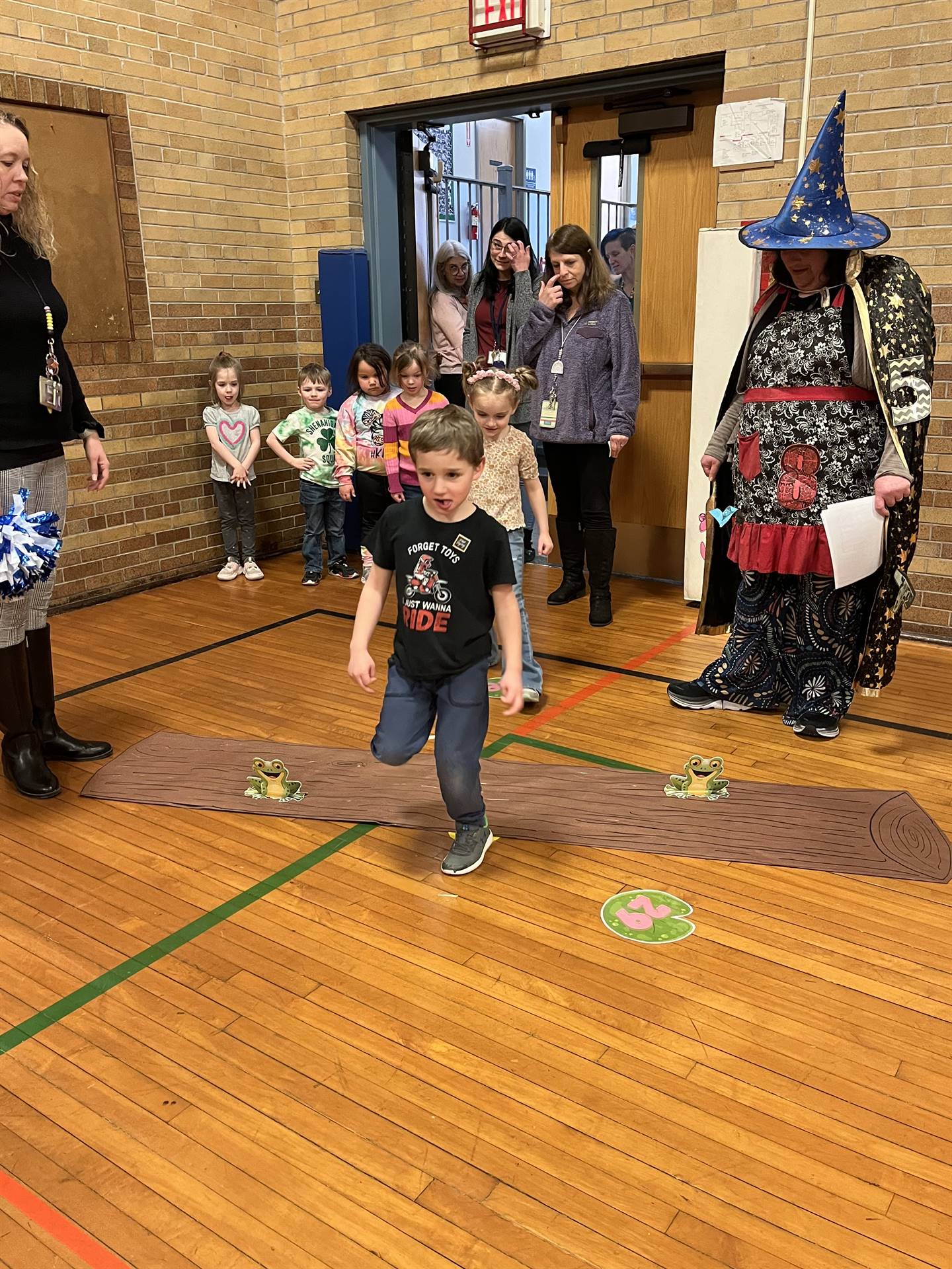 student between 2 adults leaping over a paper log.