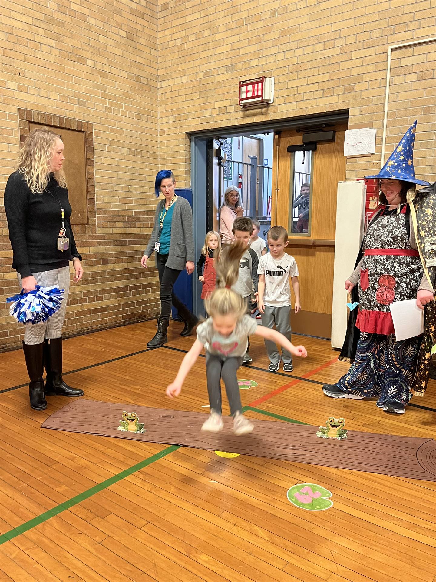 student between 2 adults leaping over a paper log.