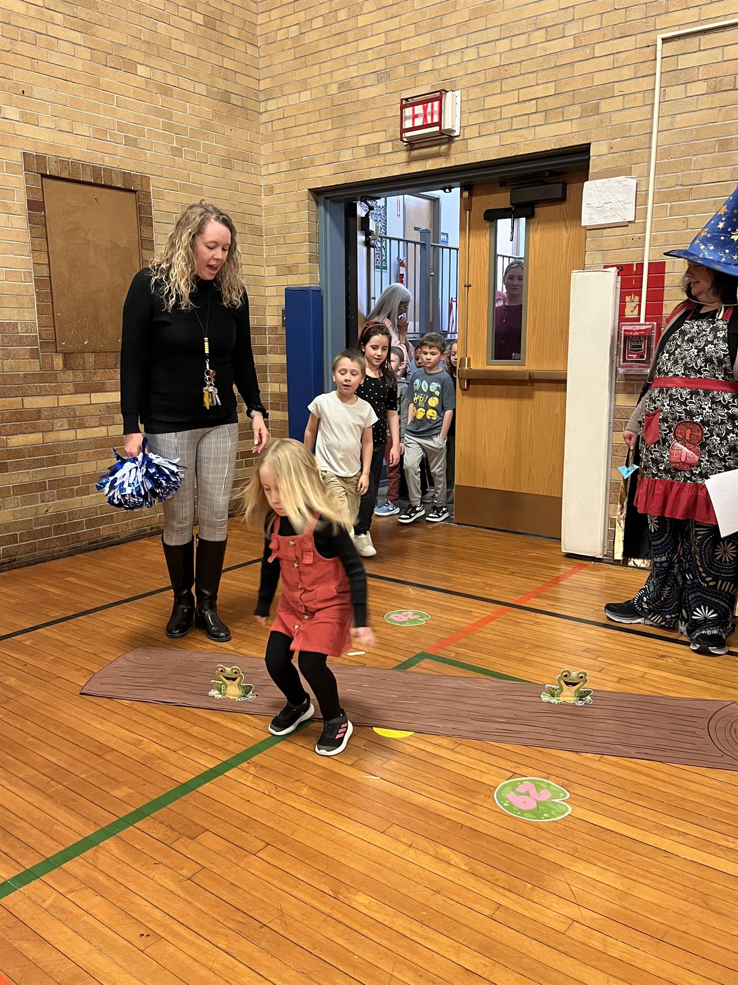 student between 2 adults leaping over a paper log.