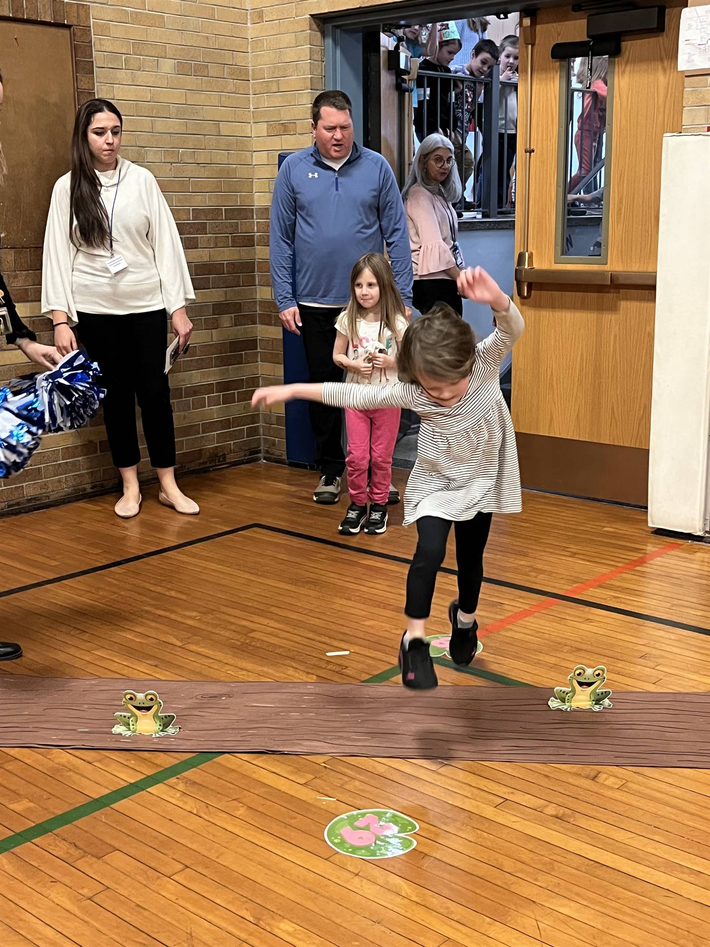 student between 2 adults leaping over a paper log.