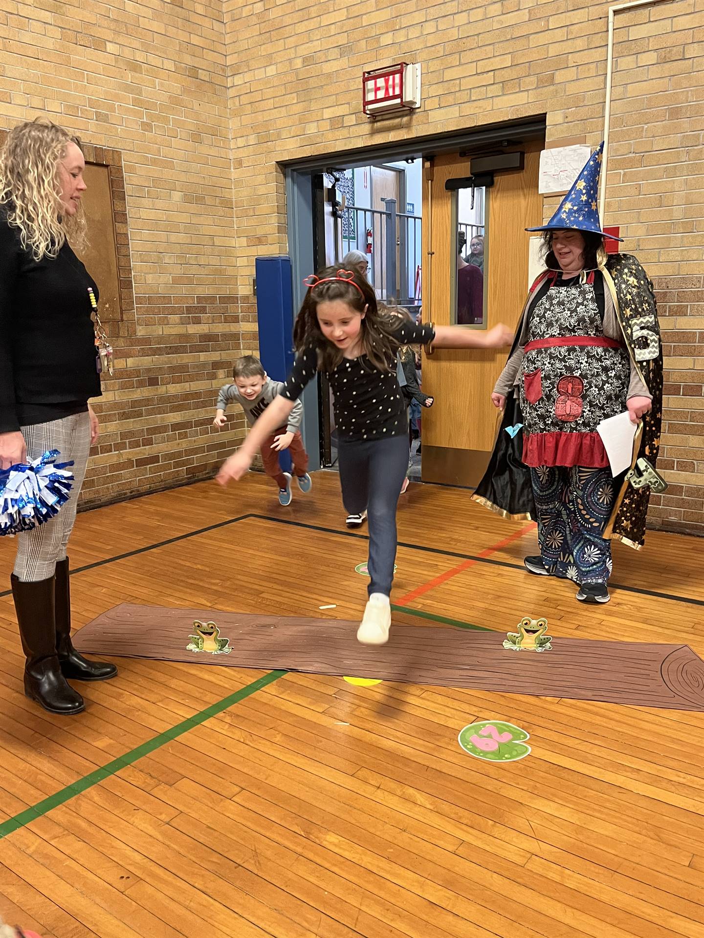 student between 2 adults leaping over a paper log.