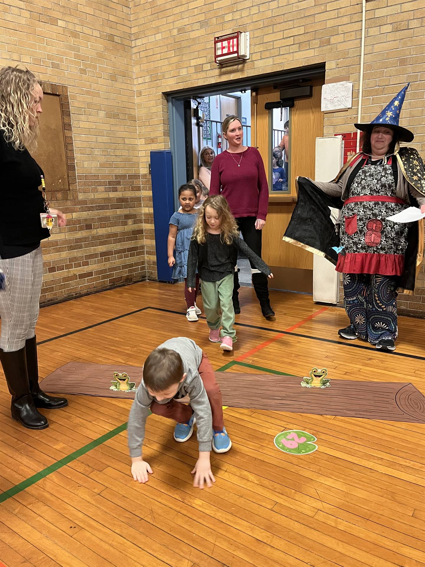 students between 2 adults leaping over a paper log.