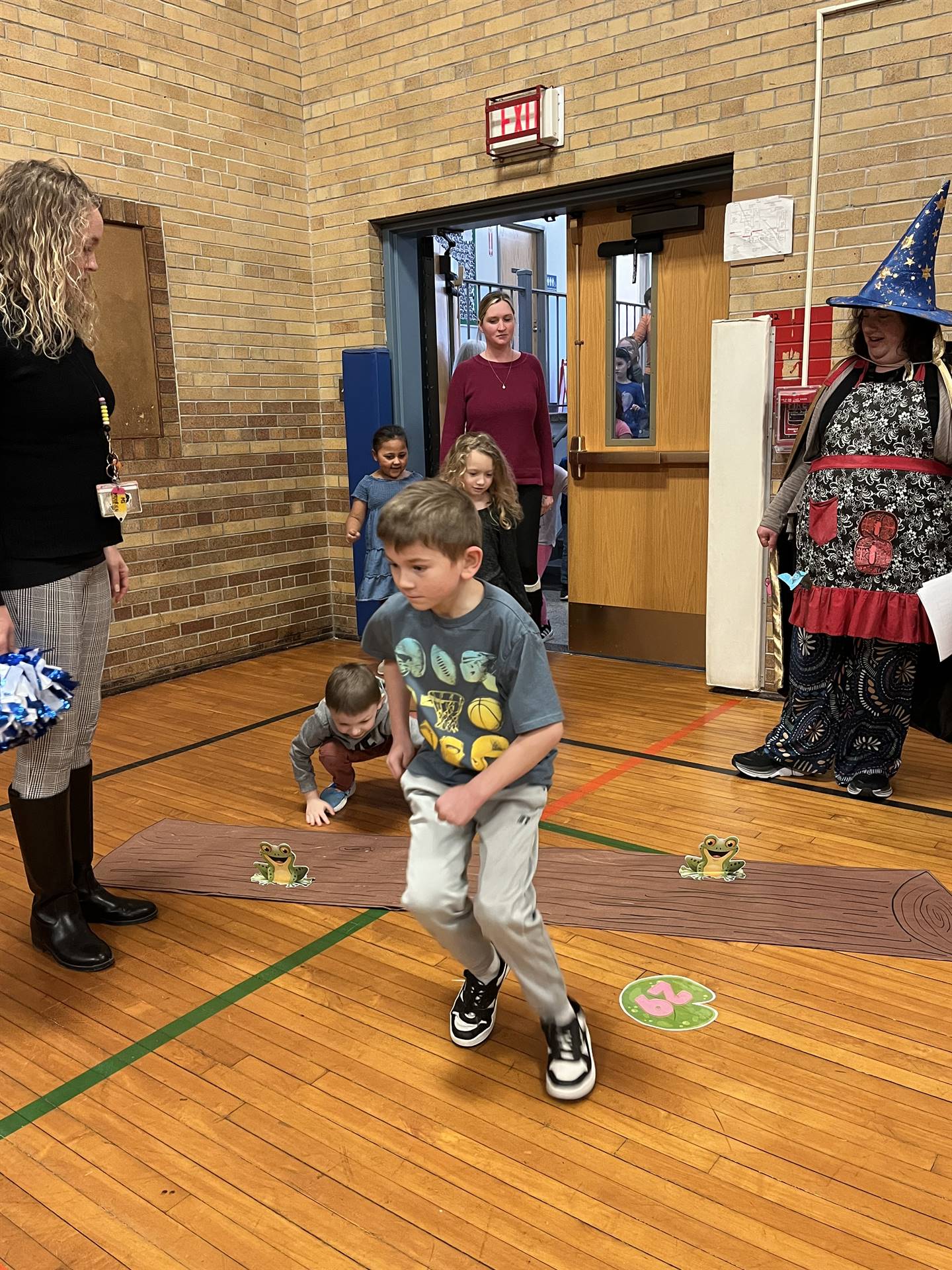 student between 2 adults leaping over a paper log.