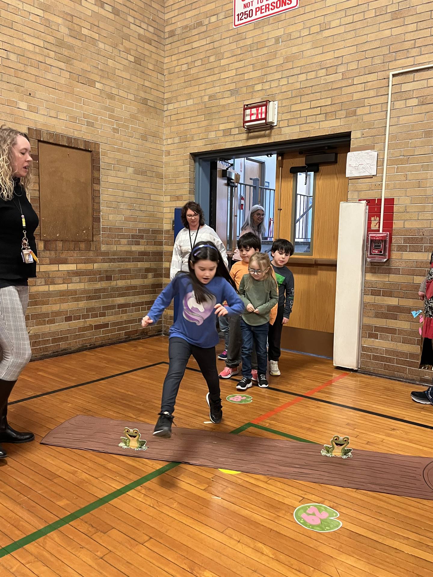 student between 2 adults leaping over a paper log.