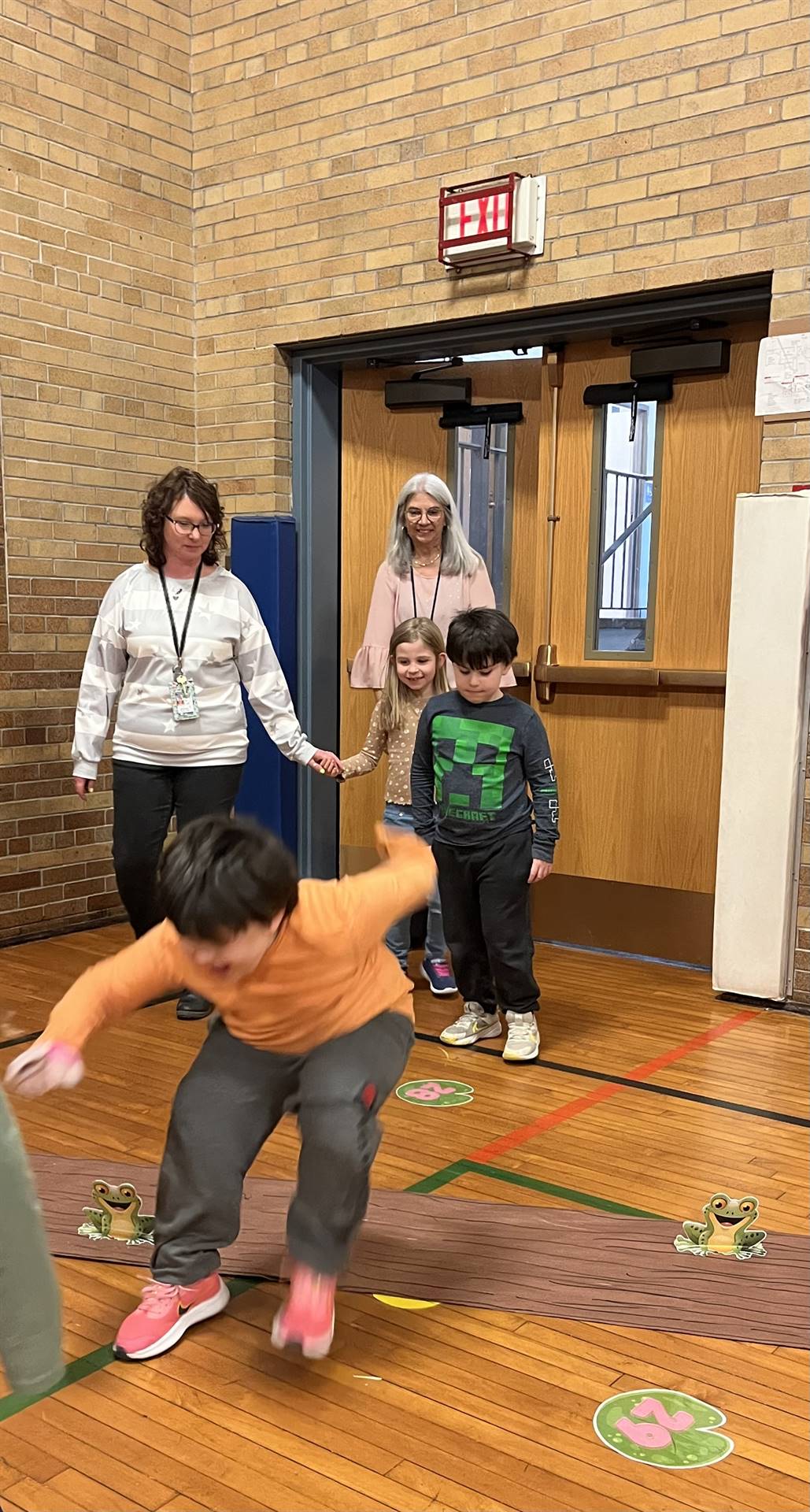 student between 2 adults leaping over a paper log.