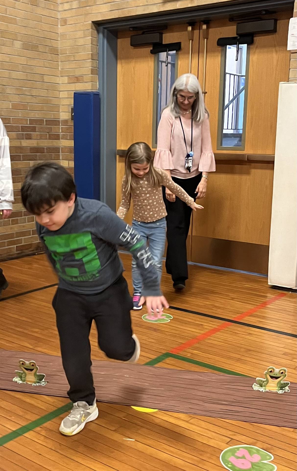 student between 2 adults leaping over a paper log.