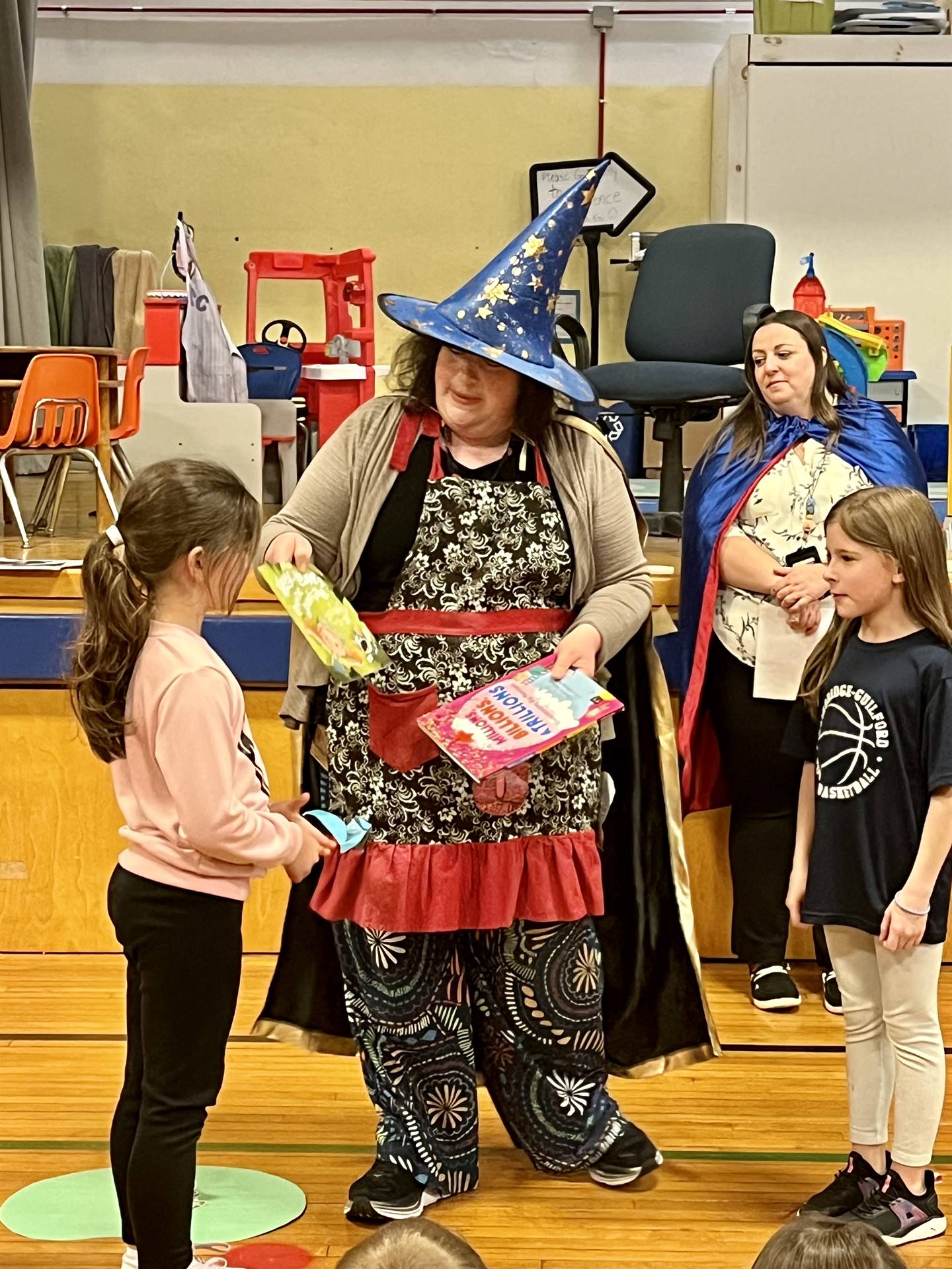 adult dressed as a wizard presenting an award to 2 students