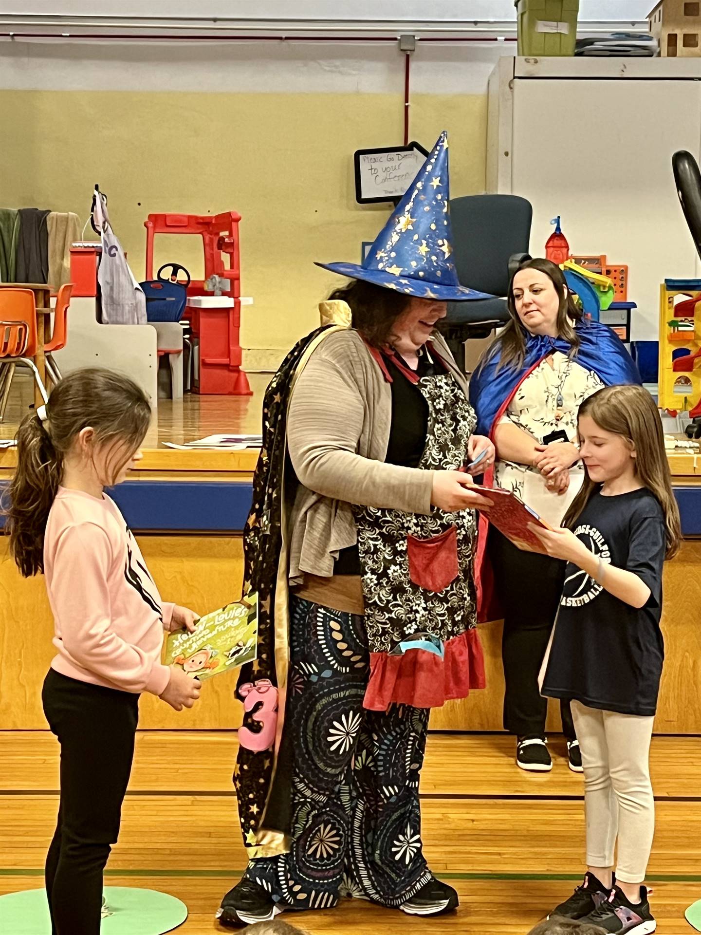 adult dressed as a wizard presenting an award to 2 students