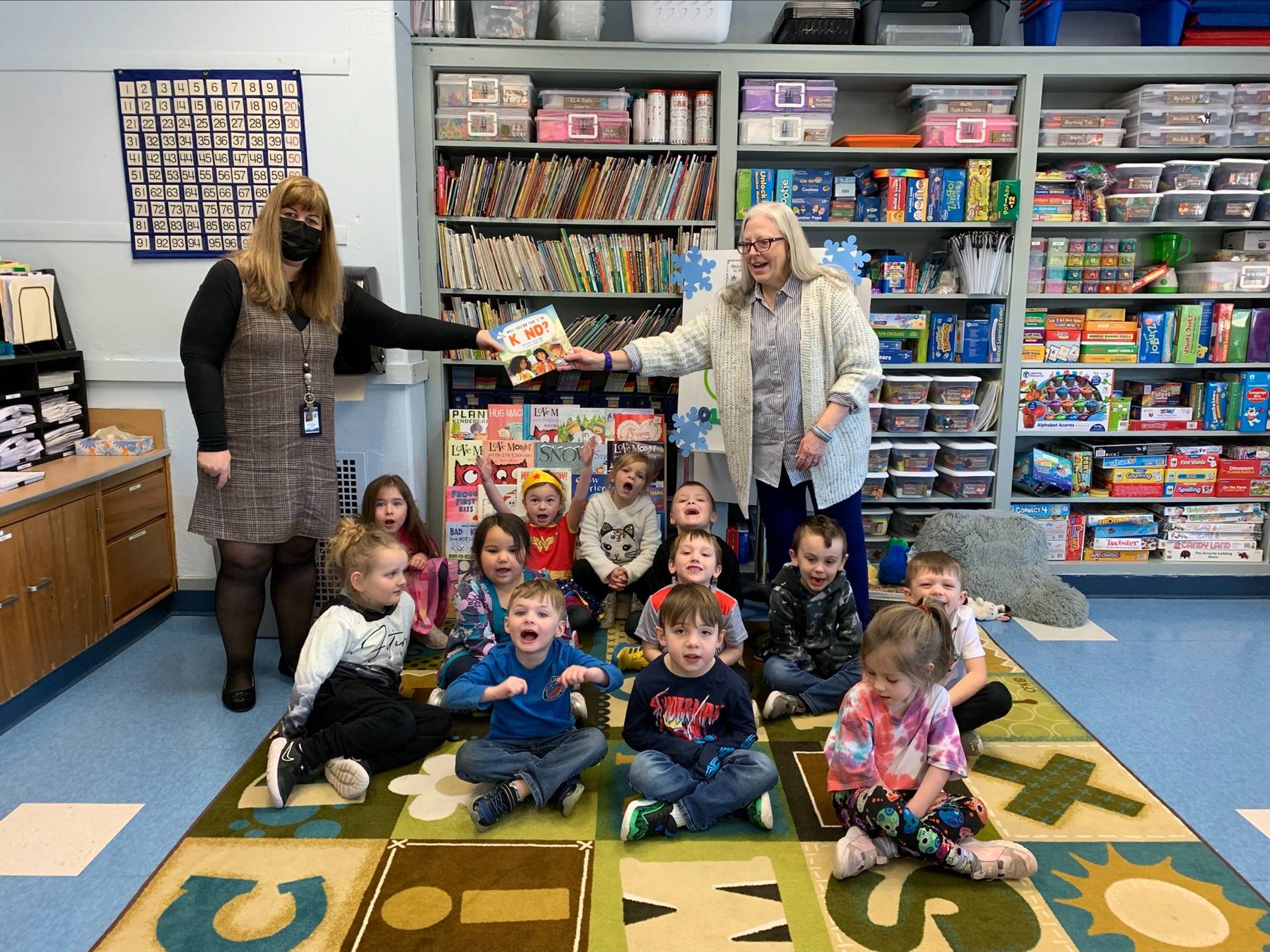 2 teachers hold up Kind book while students smile 