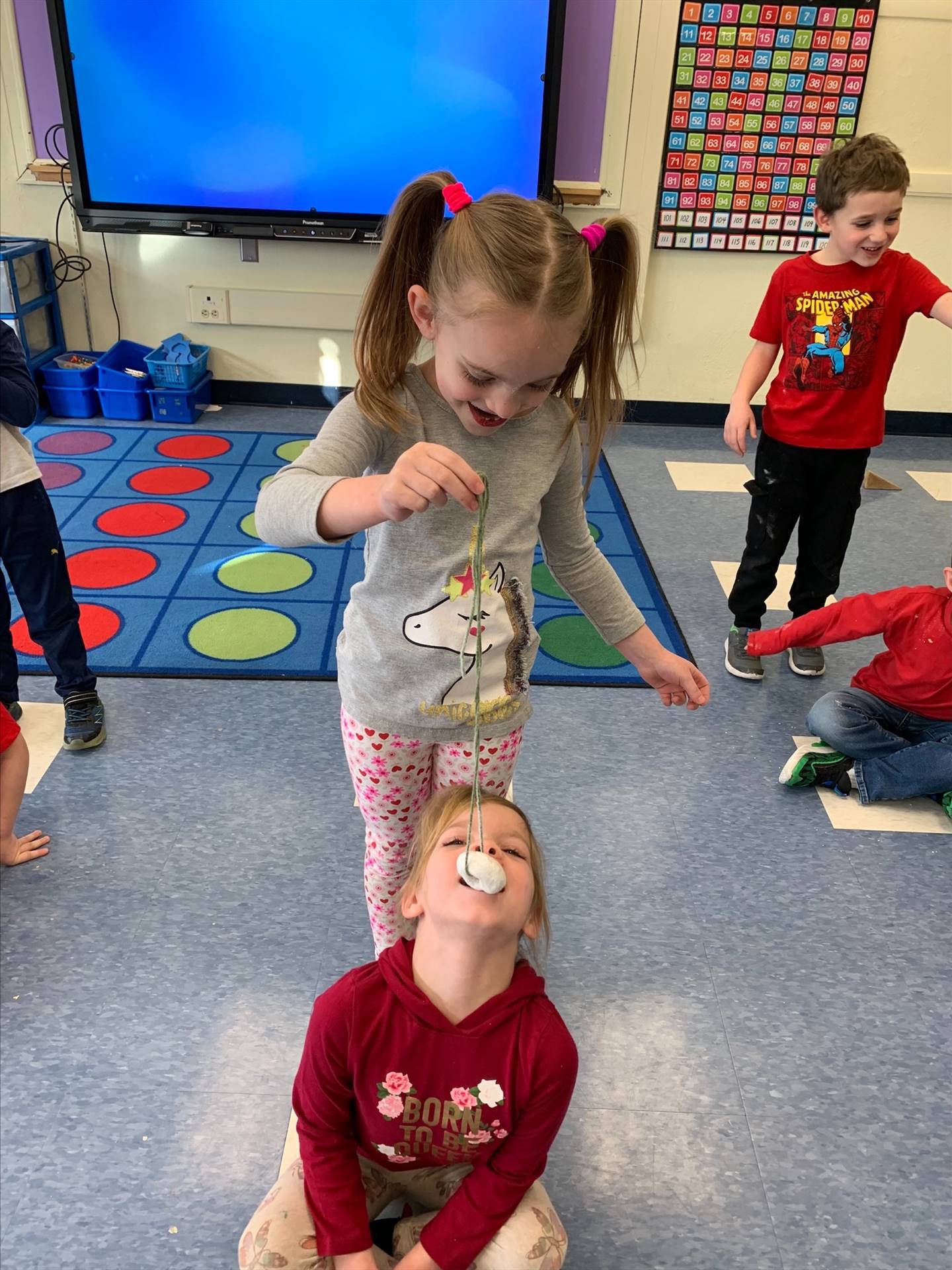 standing student hold donut on string while sitting student tries to bite it off.