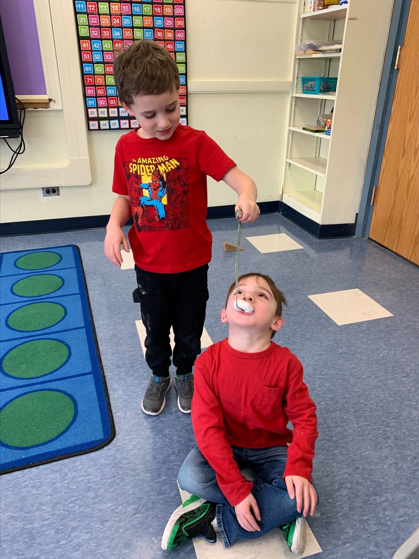 standing student hold donut on string while sitting student tries to bite it off.