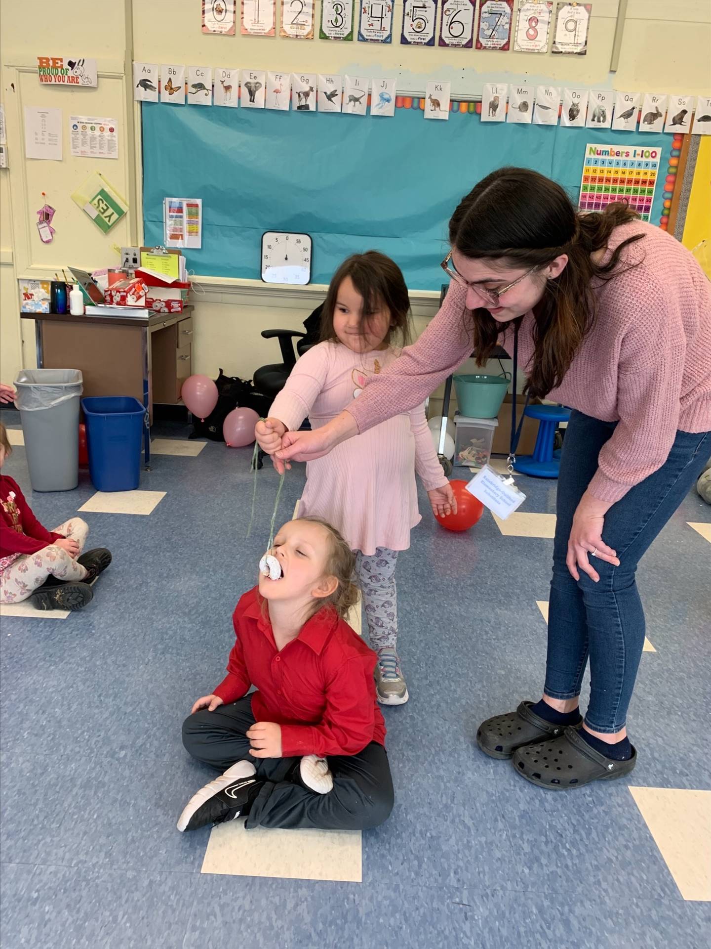 standing student hold donut on string while sitting student tries to bite it off.