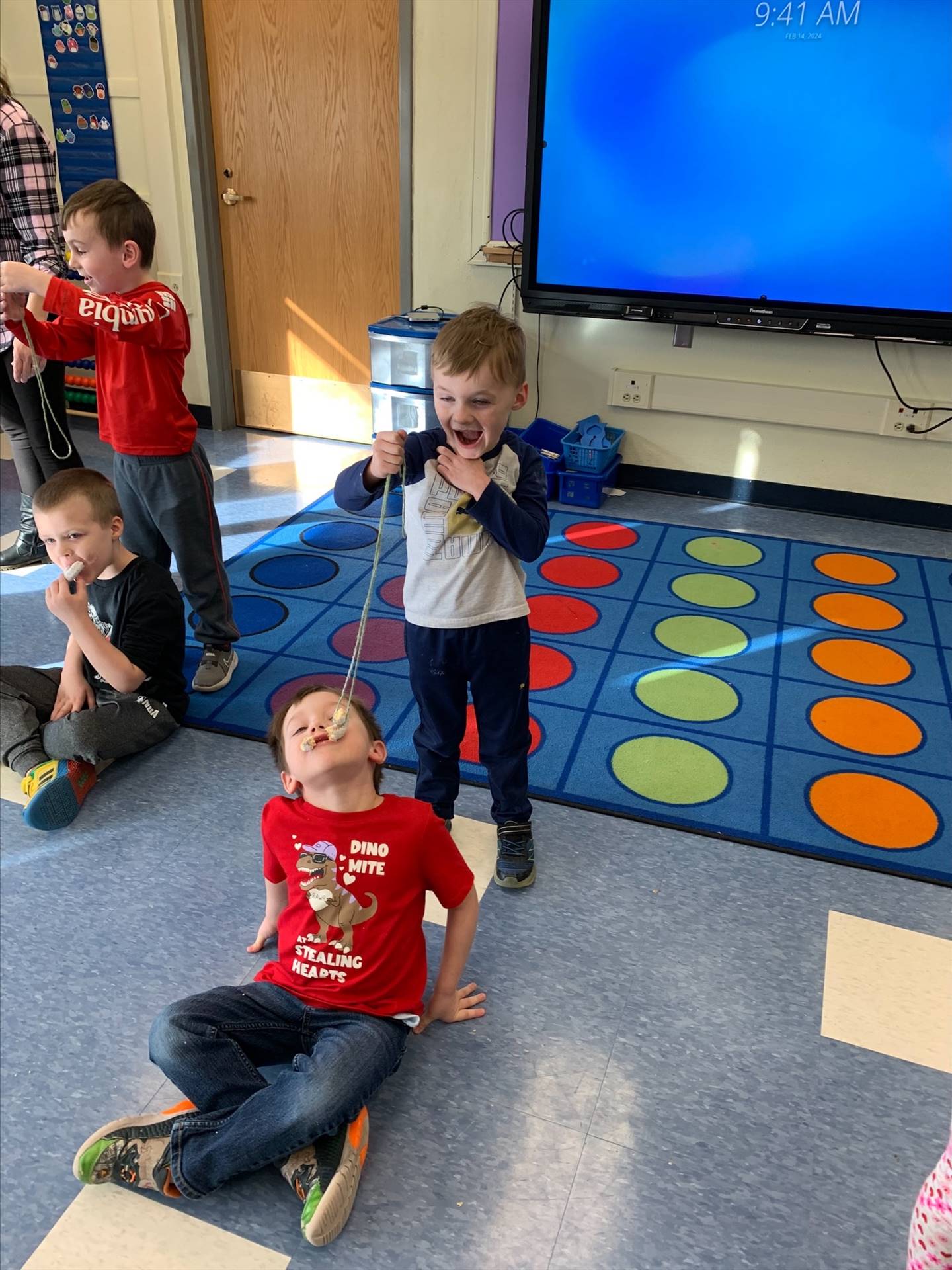 standing student hold donut on string while sitting student tries to bite it off.