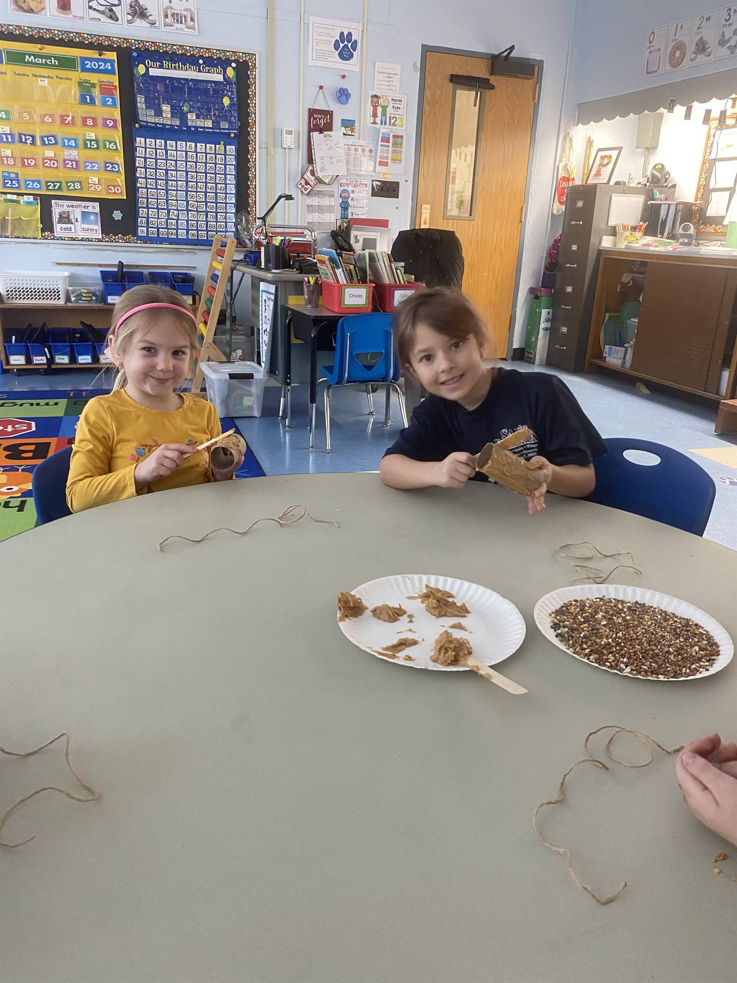 2 students smother peanut butter on tubes and roll in bird seed. 