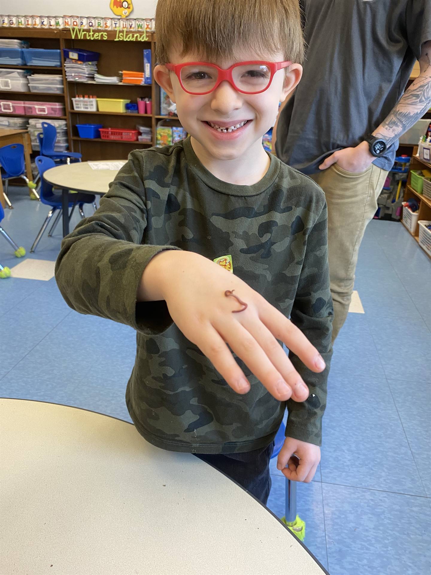 a student smiles as a worm crawls on his hand.