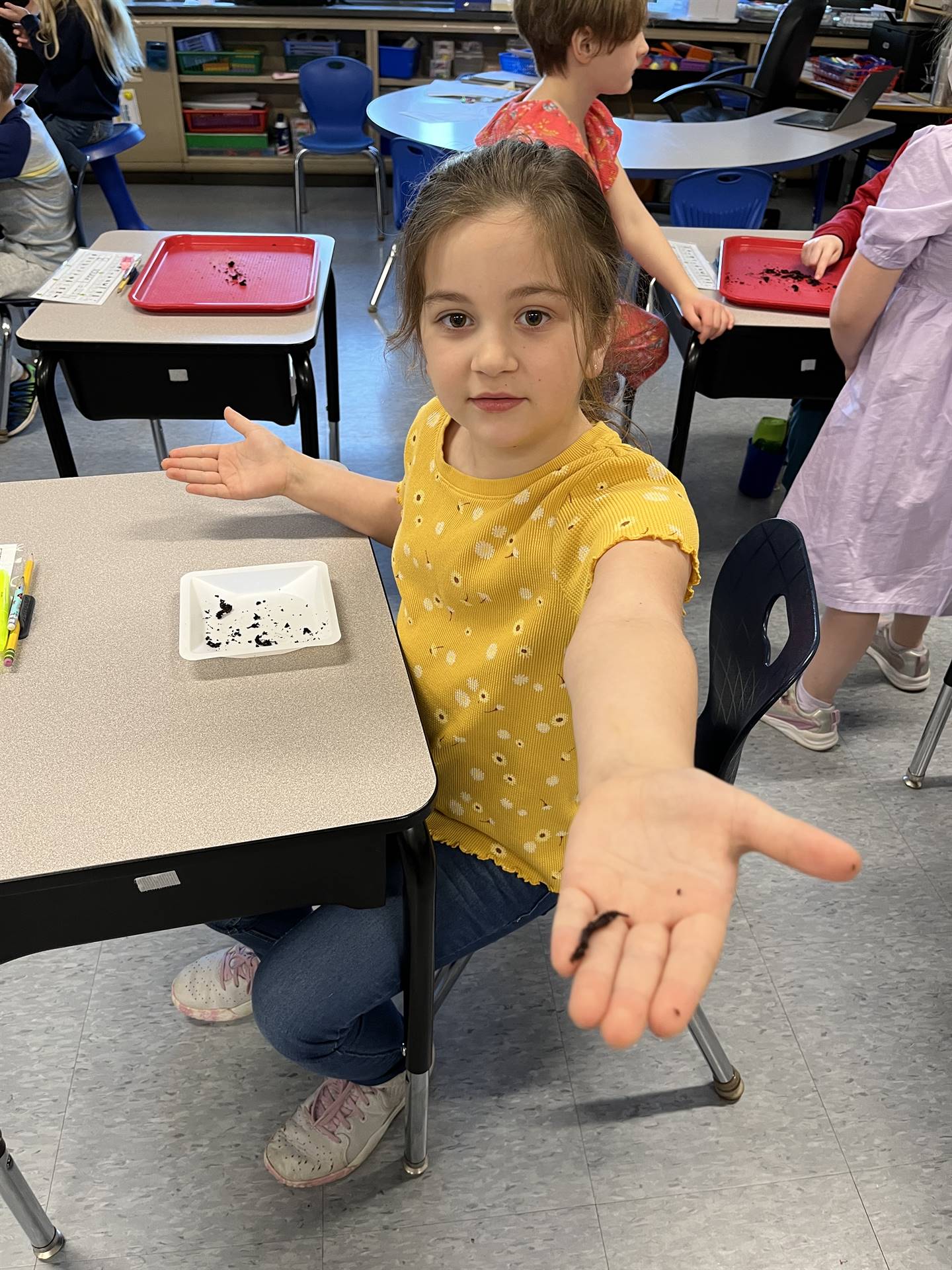 a student watches as a worm crawls on her hand