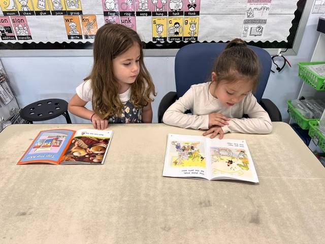 a first grader reads to a kindergarten buddy