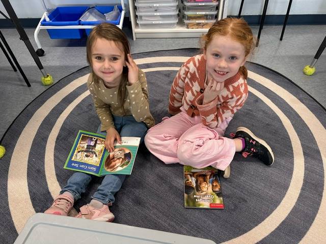 a first grader reads to a kindergarten buddy