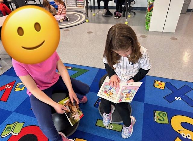 a first grader reads to a kindergarten buddy