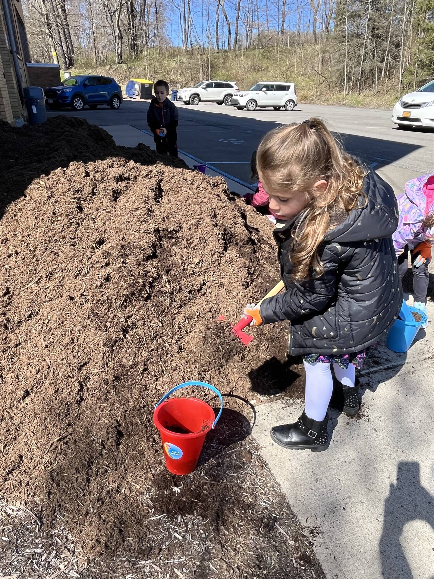 a student shovels mulch in a red pail.