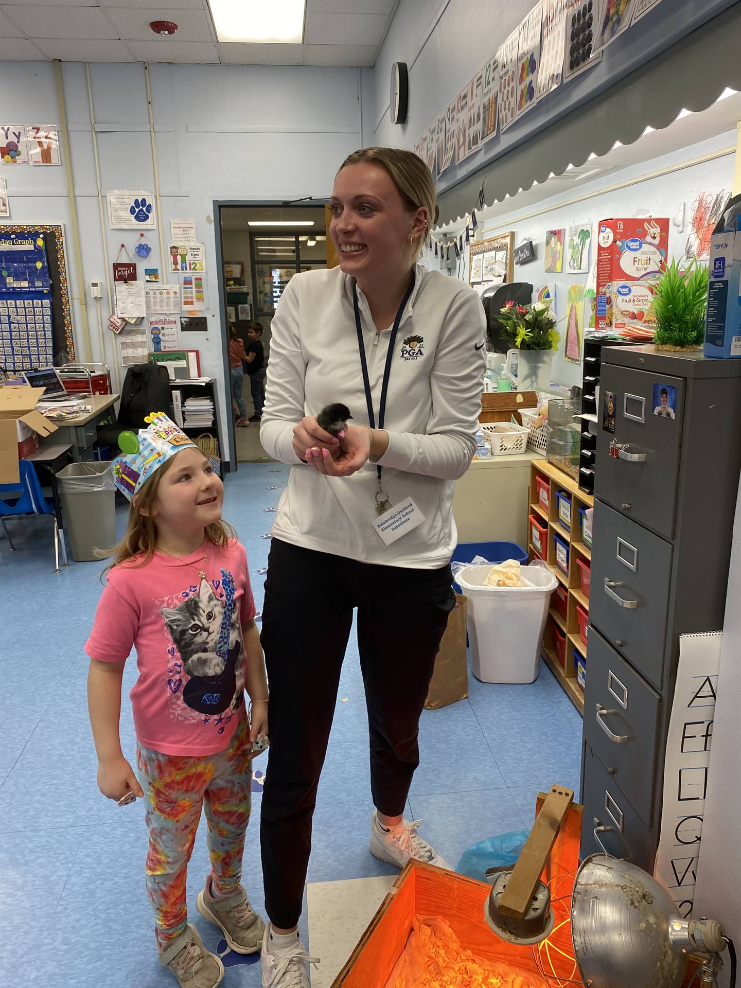 an adult holds a chick while a student observes.