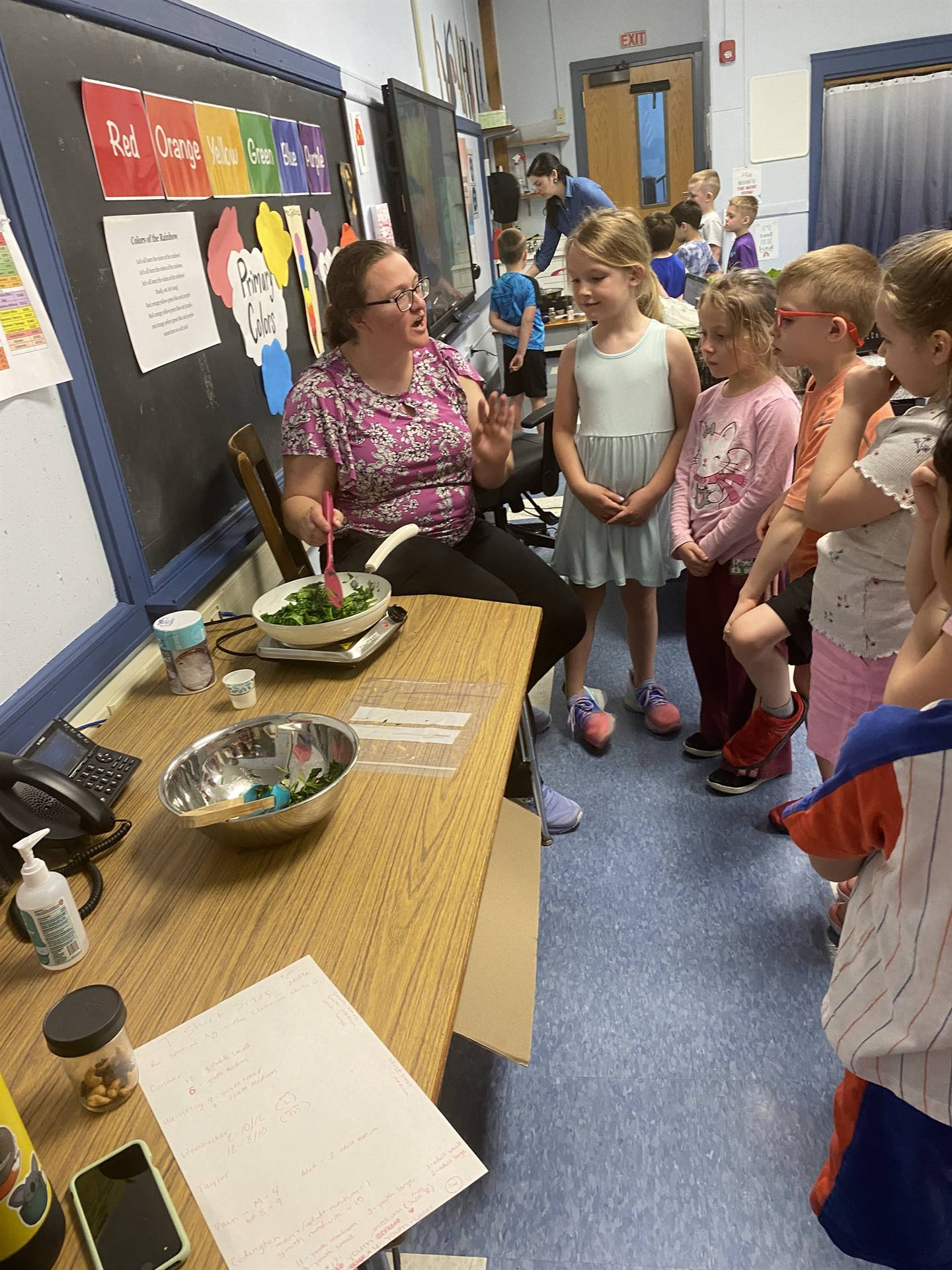 an adult cooking green plants while students observe.