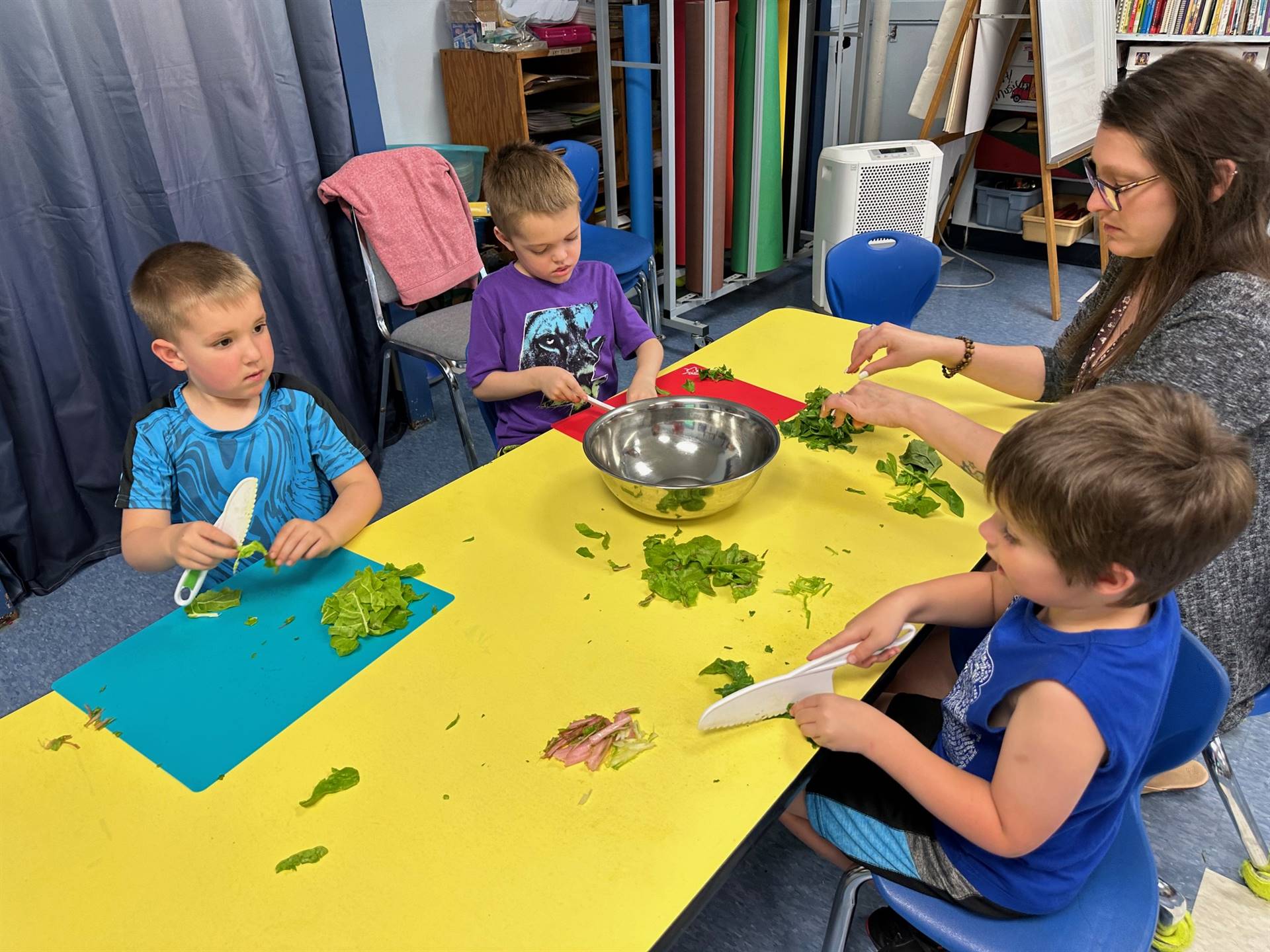 2 students ripping up swiss chard greens and cutting stems into a bowl.