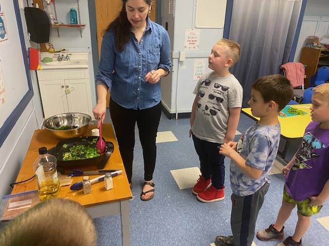 teacher cooking greens while students observe.