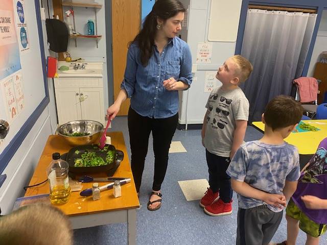 teacher cooking greens while students observe.