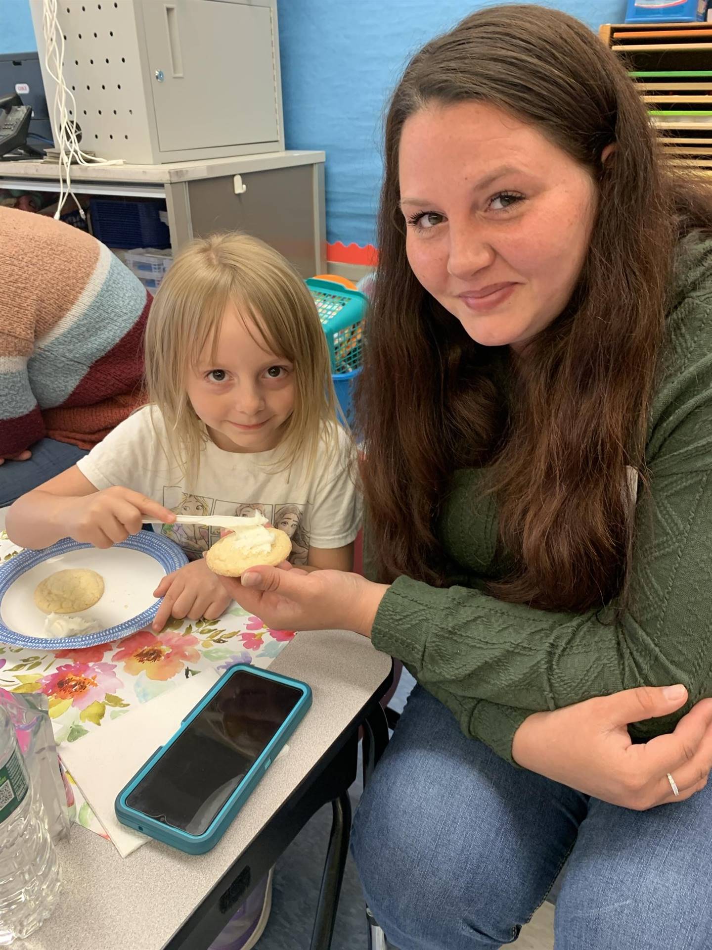 student spreading frosting on a cookie adult is holding.