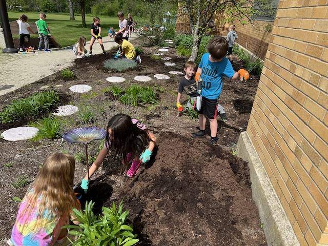students outside in pollinator garden digging and watering.