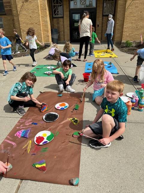 students on sidewalk painting rocks on a brown piece of paper.