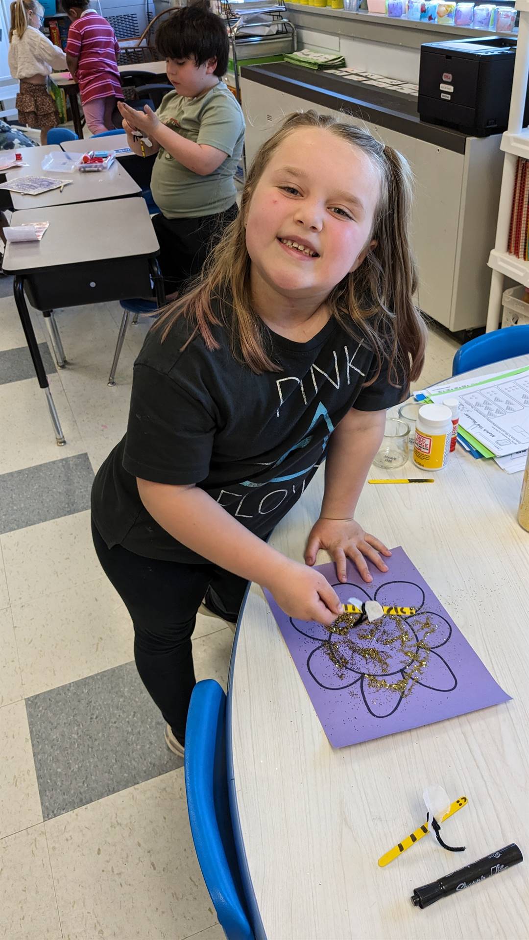 a student with a crafted paper bee flies it to a paper flower.