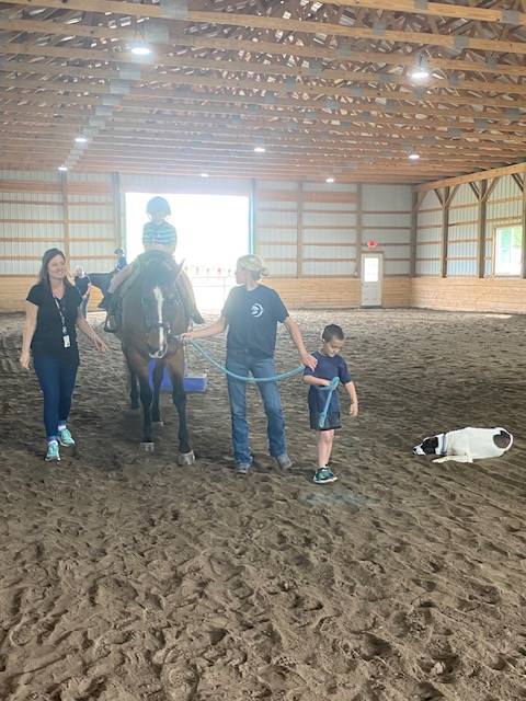 student sitting on a horse with a student and 2 adults leading