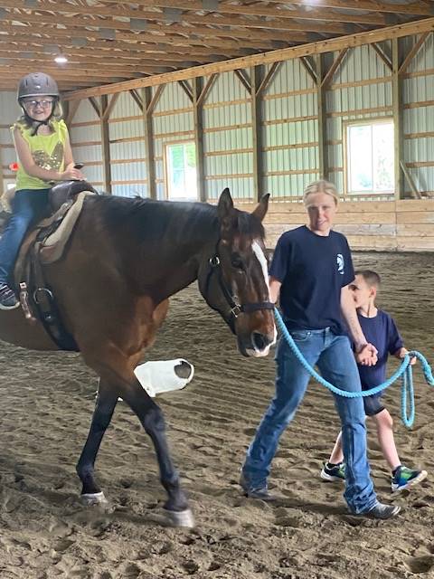 student sitting on a horse with a student and 2 adults leading