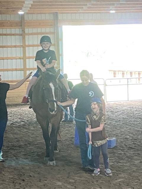 student sitting on a horse with a student and 2 adults leading