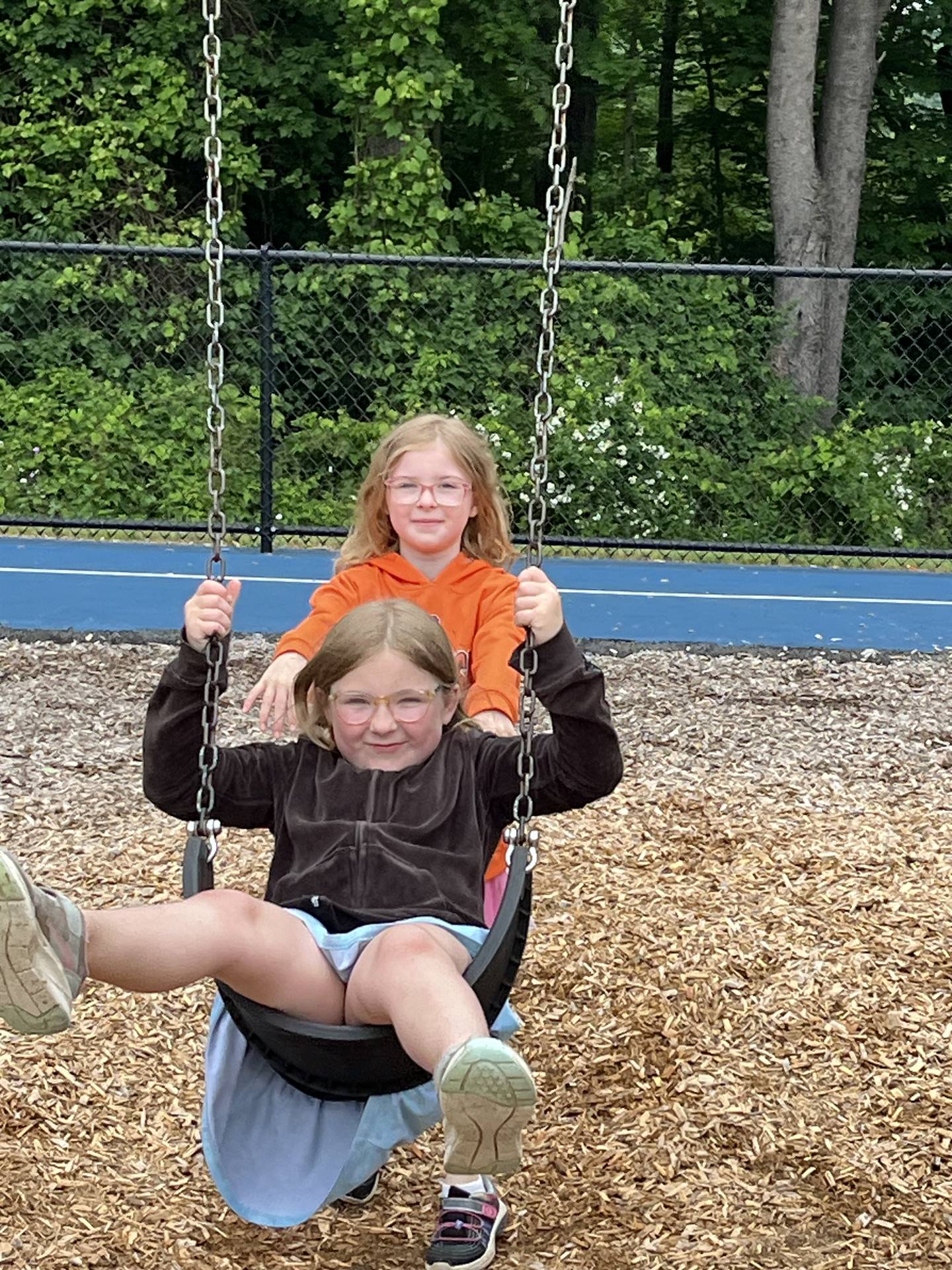 older student pushing younger student on swing