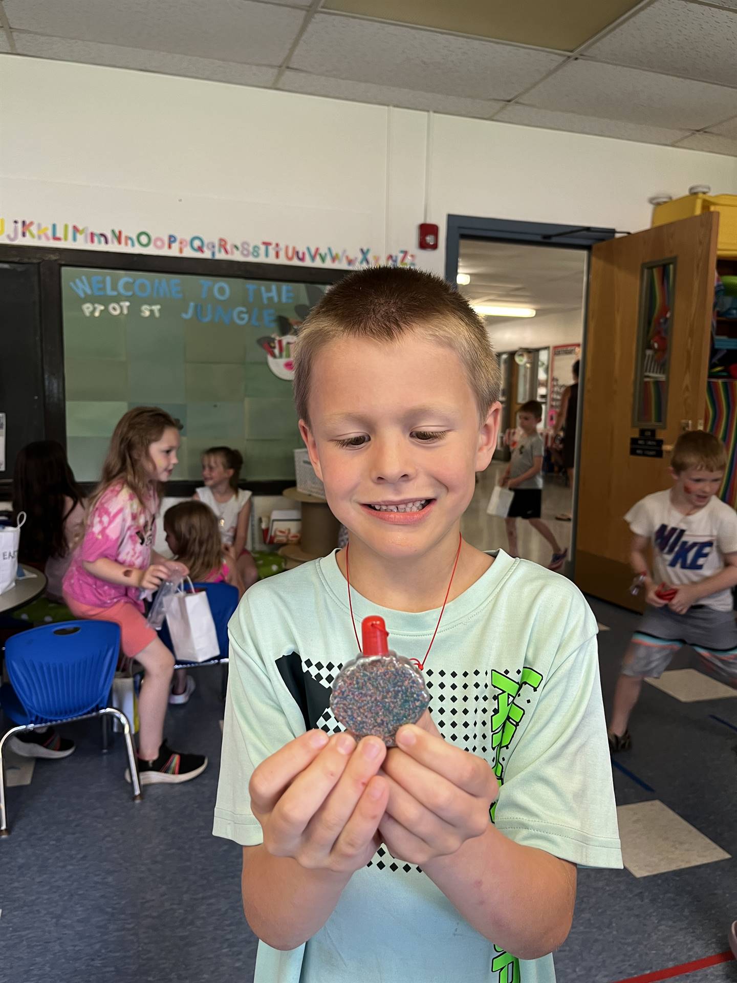 student holds up a sand art necklace he made.