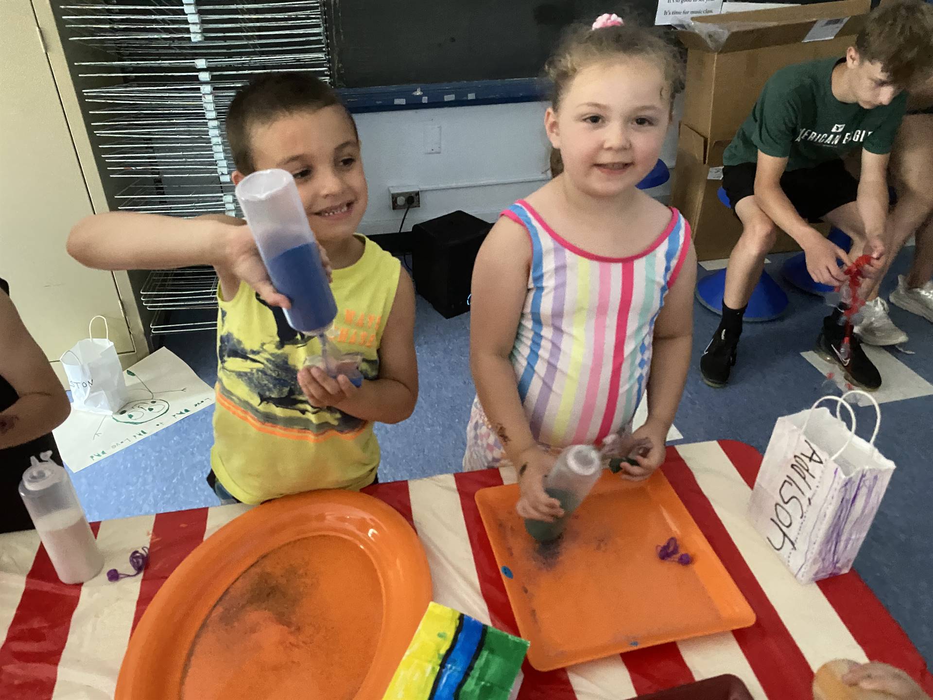 2 students pour sand out of a bottle to make a sand art craft. 