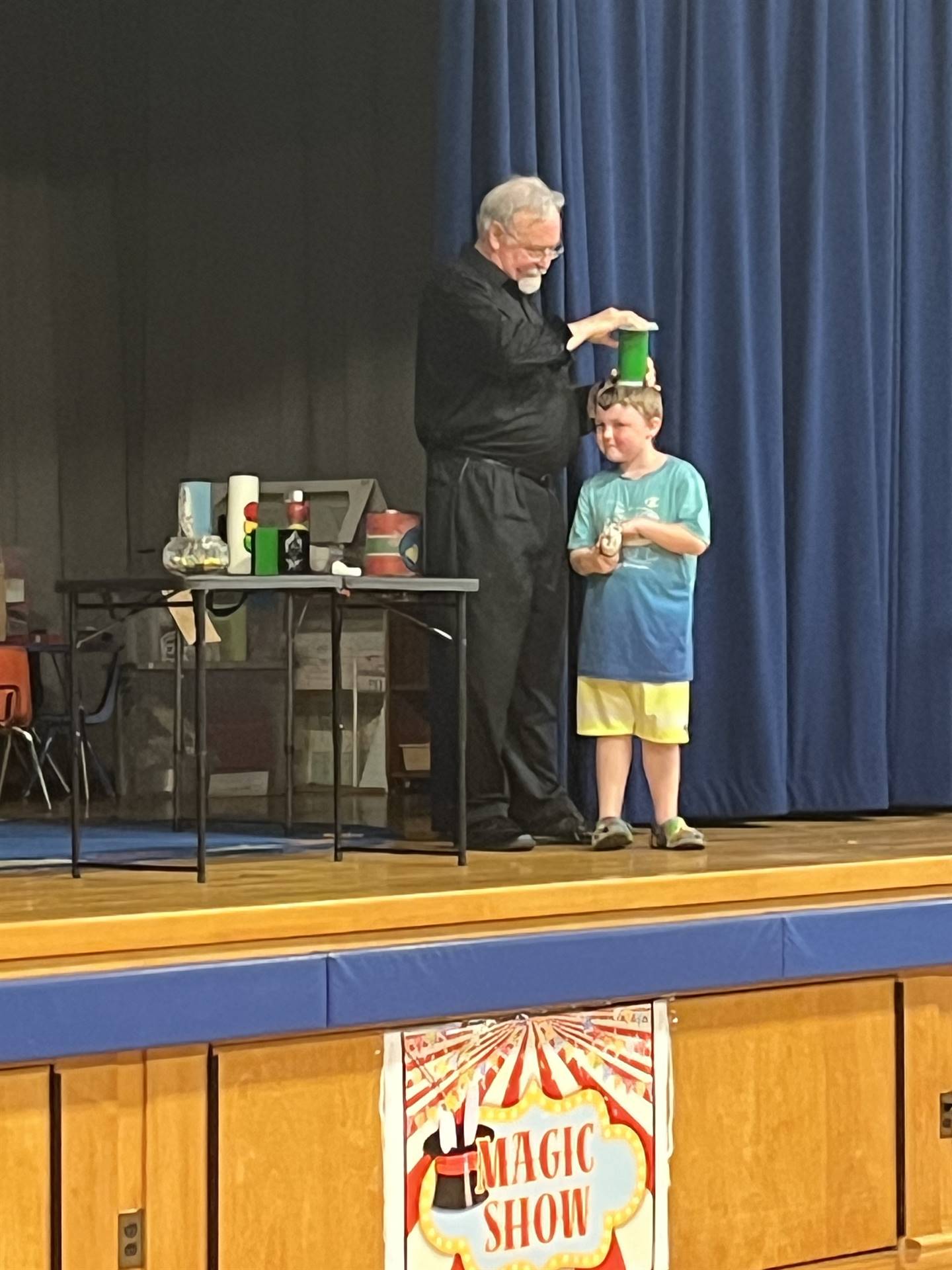 a Magician dressed in black performs a magic trick on top of a student's head.