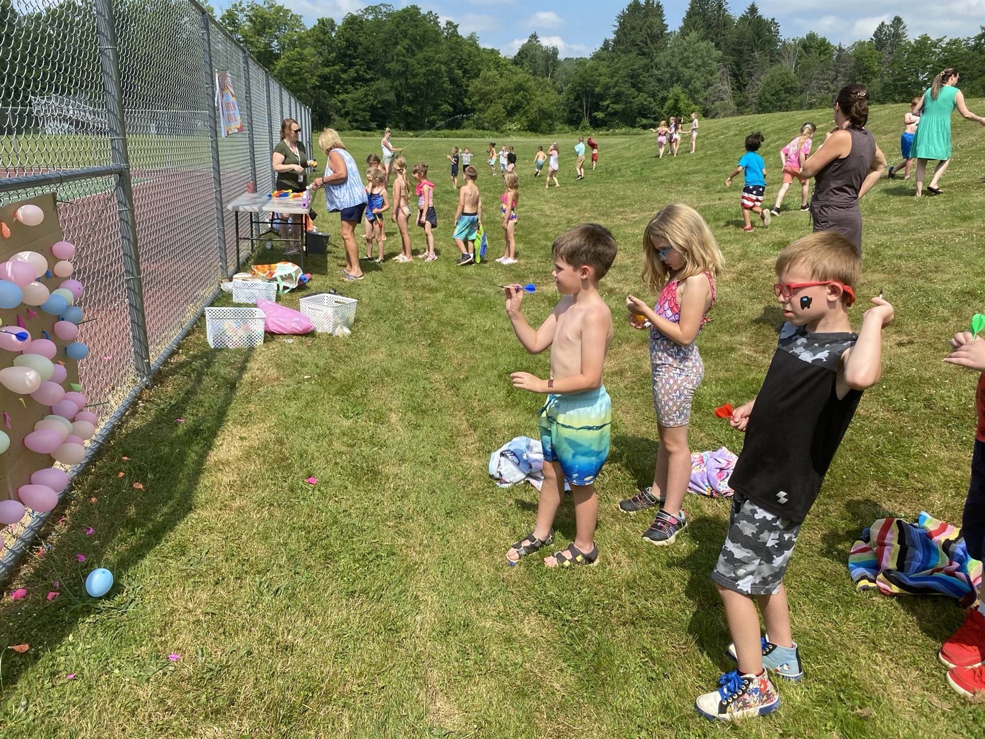 students outdoors throwing darts at balloons.