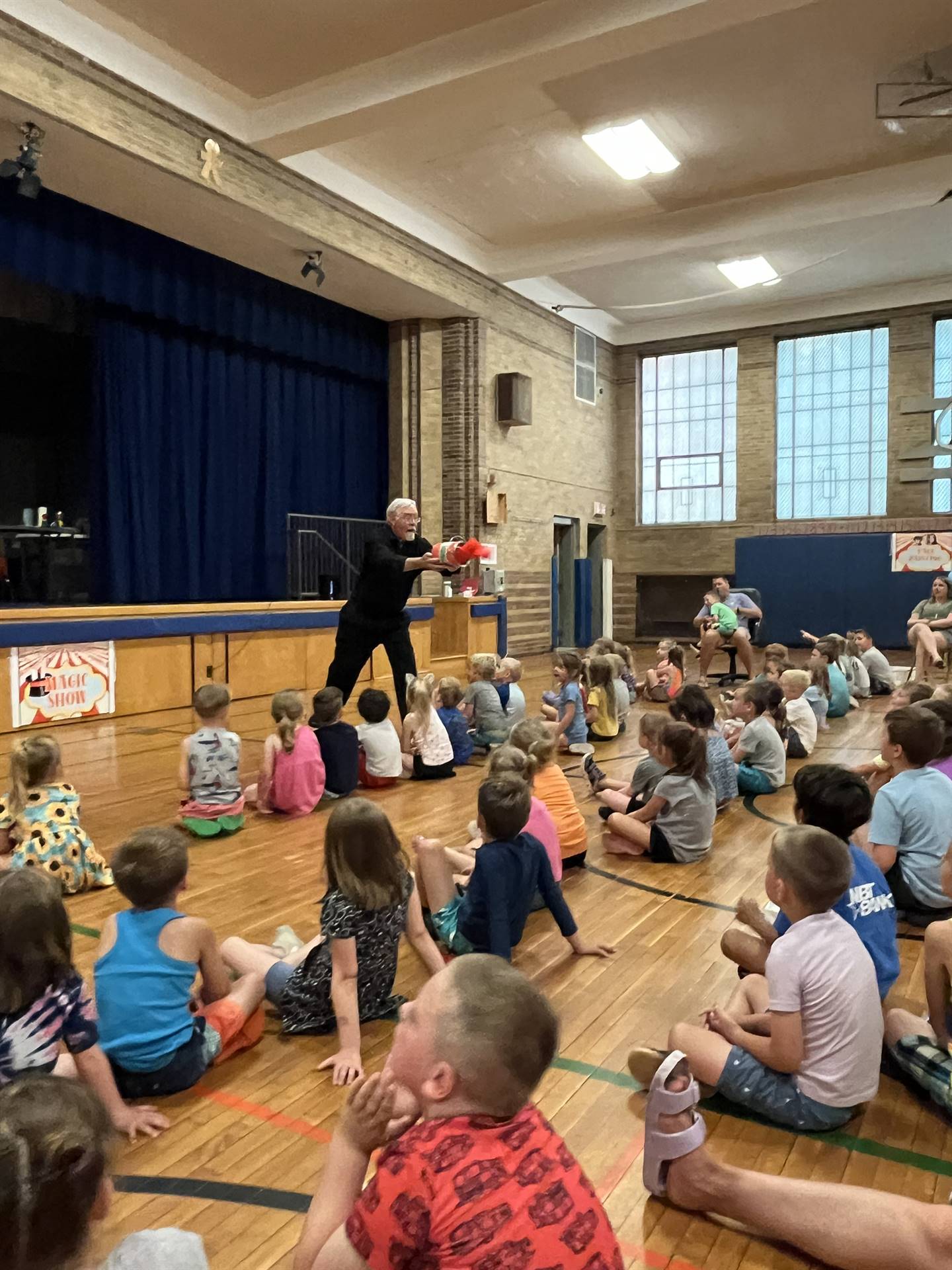 a magician pours red paint out of a paint bucket into an audience of children.