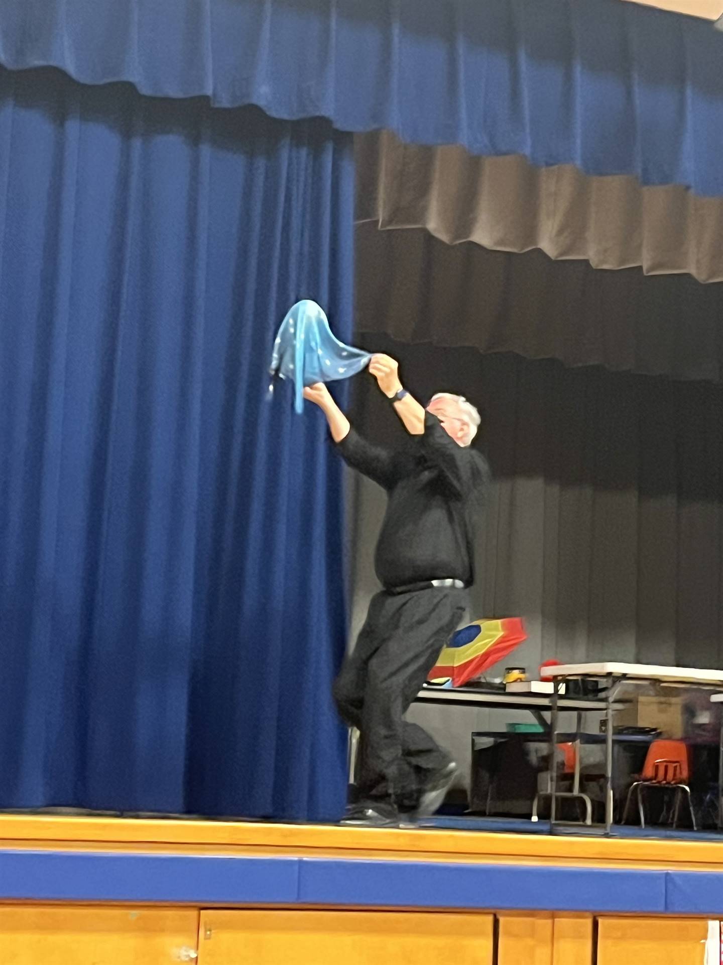 a Magician dressed in black chases a flying ball across the stage.